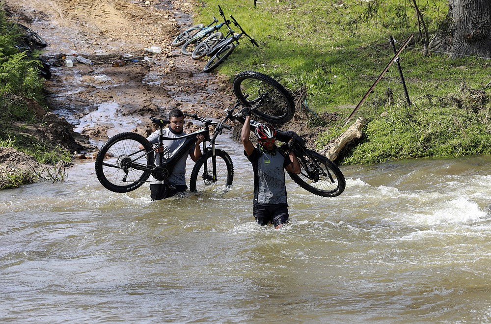 Tour guides, Colin de Wet and Severiano Tamboer, who work for tour operator Raino Bolz, cross a river during an adventure e-bike tour, between Stellenboschon and the Boschendal Estate near, Cape Town South Africa, Friday Sept. 4, 2020. Africa's tourism sector is struggling to cope with the drop in international travel caused by the COVID-19 pandemic. The World Travel and Tourism Council estimates the drop in travel caused by the COVID-19 pandemic will see Africa lose between $53 billion and $120 billion in contributions to its GDP in 2020. (AP Photo/Nardus Engelbrecht)