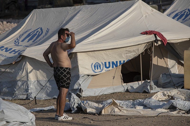 A migrant stands outside a tent at a temporary camp near Mytilene town, on the northeastern island of Lesbos, Greece, Saturday, Sept. 12, 2020. Greek authorities have been scrambling to find a way to house more than 12,000 people left in need of emergency shelter on the island after the fires deliberately set on Tuesday and Wednesday night gutted the Moria refugee camp. (AP Photo/Petros Giannakouris)