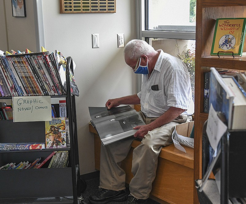 Jim North, of Hot Springs, flips through a book while sitting in a window sill at the Garland County Library in its book room, containing books for sale on Monday. - Photo by Grace Brown of The Sentinel-Record story.lead_photo.caption