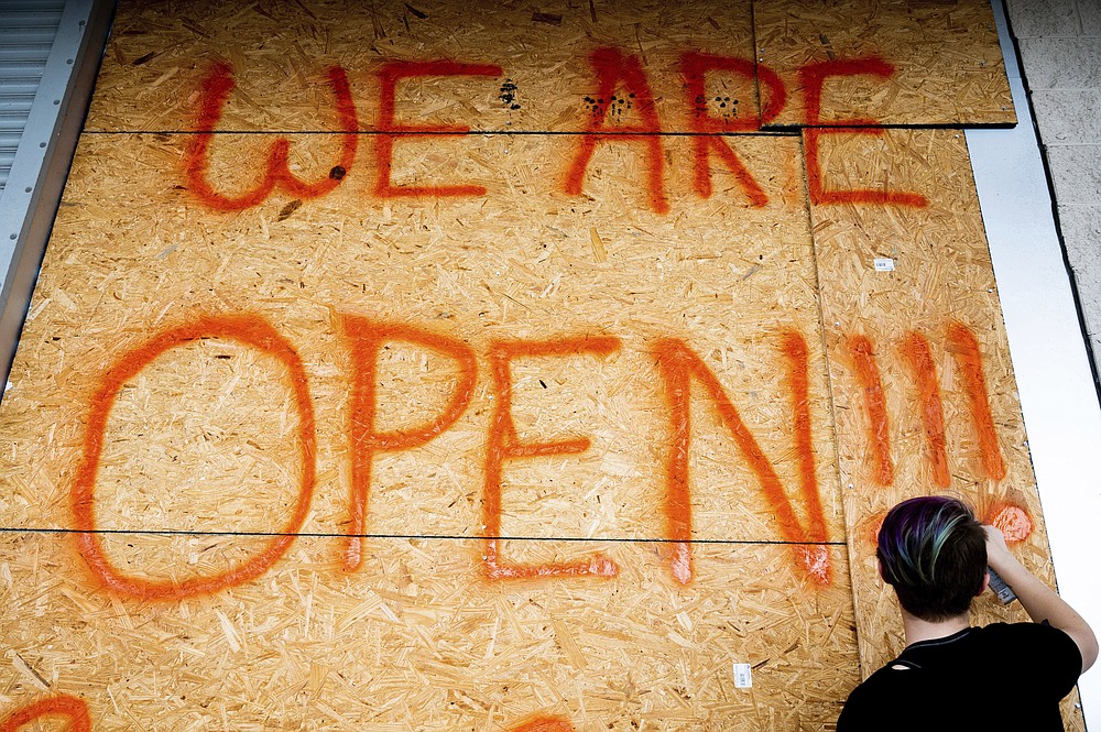 A Dirt Cheap store employee spray paints the day's business hours onto a board of plywood in anticipation of Hurricane Sally making landfall, in Bay St. Louis, Miss., on Monday, Sept. 14, 2020. Gulf coast residents are making last minute purchases as they prepare for the expected severe weather from the hurricane. (Lukas Flippo/The Sun Herald, via AP)