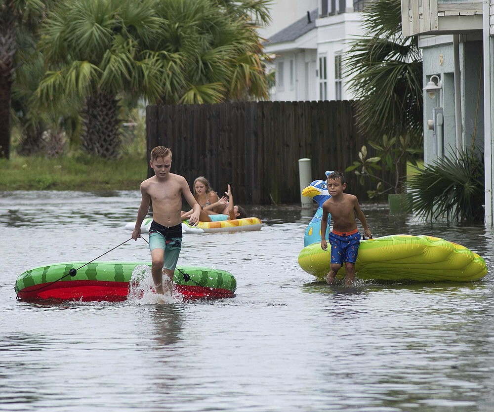 Landon Suarez and Landon Campbell turn the flooded parking lot of the Bahia-Paz condos into a waterpark, Monday, Sept. 14, 2020, in Pensacola Beach, Fla. Storm-weary Gulf Coast residents rushed to finish last-minute preparations Monday as Hurricane Sally chugged slowly through warm Gulf waters. Forecasters predicted the biggest threat is flooding, with as much as two feet of rain falling in some areas. (Tony Giberson/Pensacola News Journal via AP)