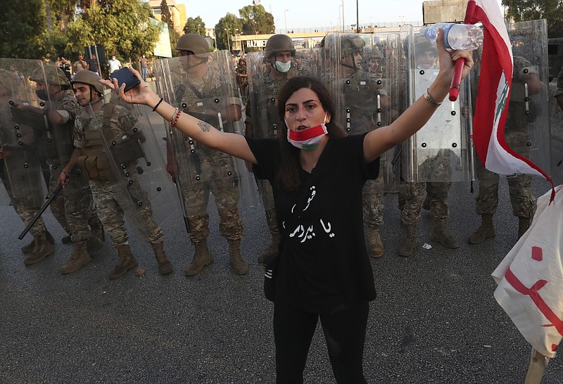 An anti-government protester tries to calm down other protesters, as she stands in front of Lebanese soldiers who bloc a road that links to the presidential palace, during a protest against the Lebanese President Michel Aoun, in Baabda east of Beirut, Lebanon, Saturday, Sept. 12, 2020. Soldiers fired rubber bullets and live rounds in the air to disperse hundreds of protesters trying to march to the presidential palace during an anti-government demonstration. (AP Photo/Bilal Hussein)