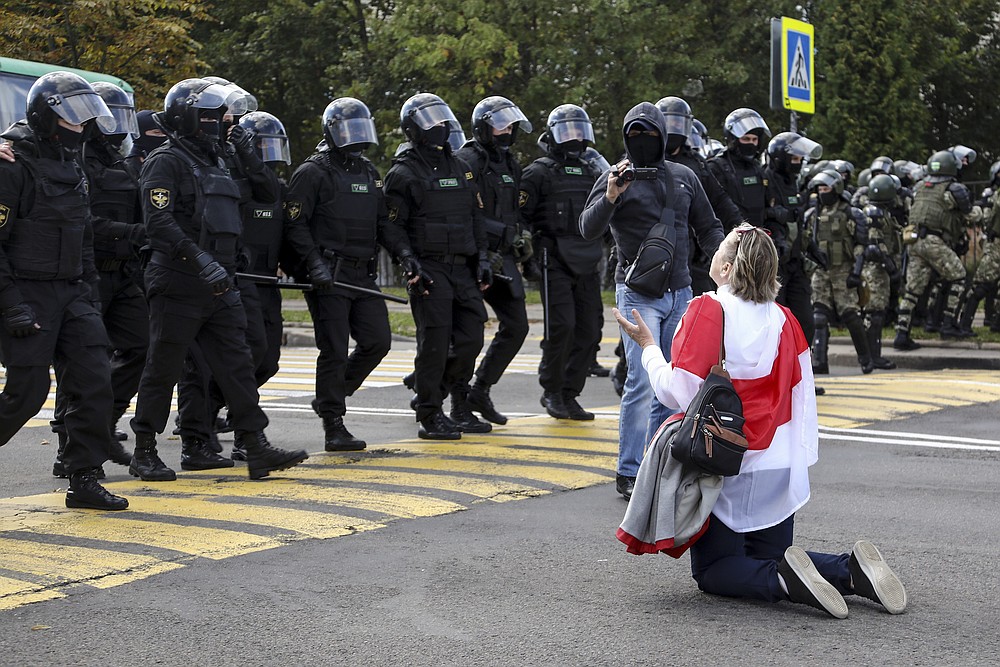 A woman covered herself by an old Belarusian national flag kneels in front of a riot police line as they block Belarusian opposition supporters rally protesting the official presidential election results in Minsk, Belarus, Sunday, Sept. 13, 2020. Protests calling for the Belarusian president's resignation have broken out daily since the Aug. 9 presidential election that officials say handed him a sixth term in office. (TUT.by via AP)