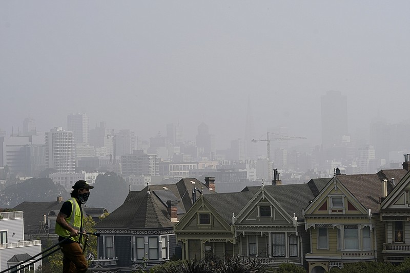 A worker cleans grass at Alamo Square Park as smoke from wildfires and fog obscures the skyline above the "Painted Ladies," a row of historical Victorian homes, in San Francisco, Monday, Sept. 14, 2020. (AP Photo/Jeff Chiu)