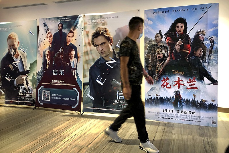 A man wearing a face mask walks past a poster for the Disney movie "Mulan" at a movie theater in Beijing, on Sept. 11, 2020. The remake of “Mulan” struck all the right chords to be a hit in the key Chinese market. Disney cast beloved actresses Liu Yifei as Mulan and removed a popular dragon sidekick in the original to cater to Chinese tastes. (AP Photo/Mark Schiefelbein)