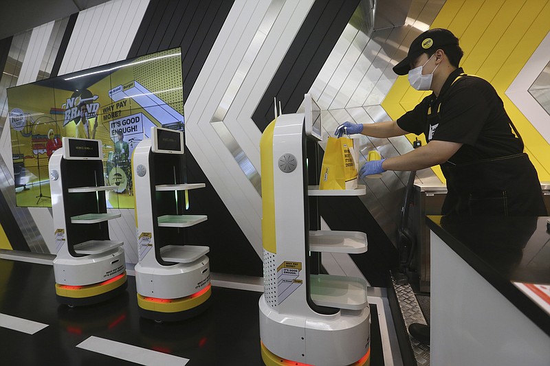 In this Sunday, Sept. 13, 2020 photo, an employee places a takeout bag with food at a robot at No Brand Burger in Seoul, South Korea. These robotic services have been seen as a selling point amid the coronavirus pandemic and its restrictions. (AP Photo/Ahn Young-joon)
