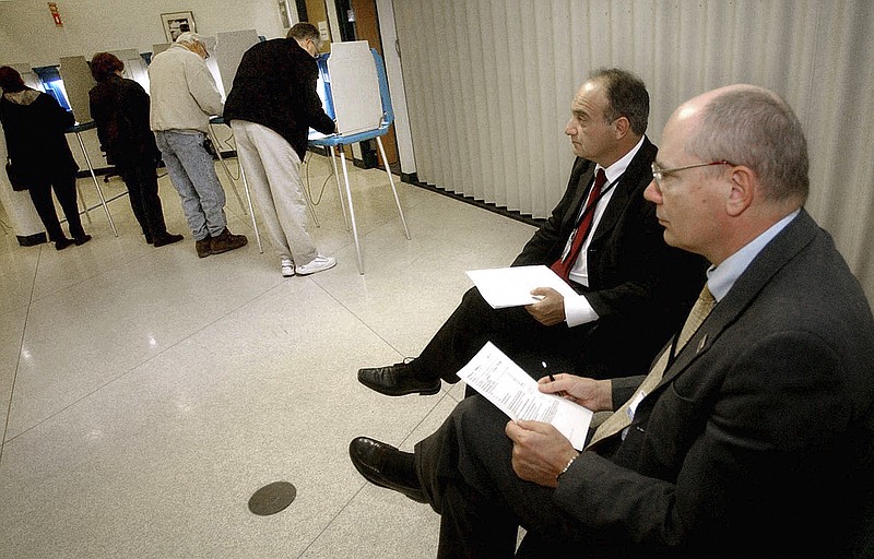 FILE - In this Nov. 2, 2004, file photo, parliamentarians Goran Lennmarker, right, of Sweden and Stavros Evagorow, of Cyprus, observe the American voting process as voters cast their ballots at Robbinsdale City Hall in Robbinsdale, Minn. The two men are members of the Organization for Security and Cooperation in Europe. Officials said Friday, Sept. 18, 2020, that due to the coronavirus pandemic, the security organization had drastically scaled back plans to send up to 500 observers to the U.S. to monitor the Nov. 3 presidential election, and now will deploy just 30. (AP Photo/Jim Mone, File)