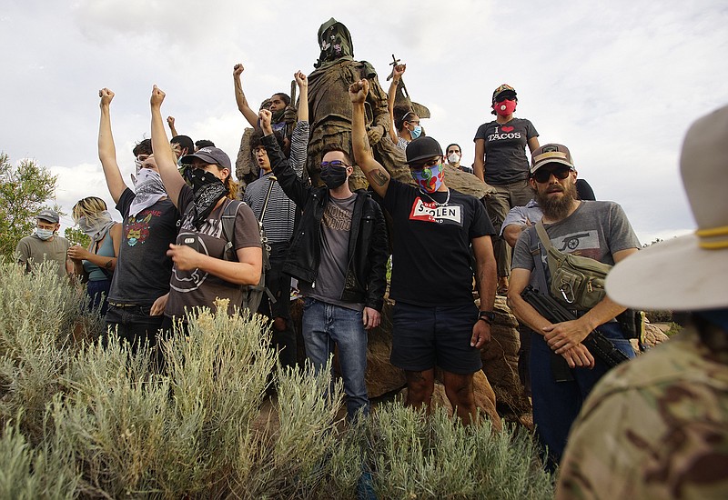 Demonstrators climb the statue of Don Juan de Onate in Old Town in Albuquerque, N.M., while an armed member of the New Mexico Civil Guard stands by during a protest calling for the removal of the likeness of the controversial New Mexico explorer Monday, June 15, 2020. (Adolphe Pierre-Louis/The Albuquerque Journal via AP)