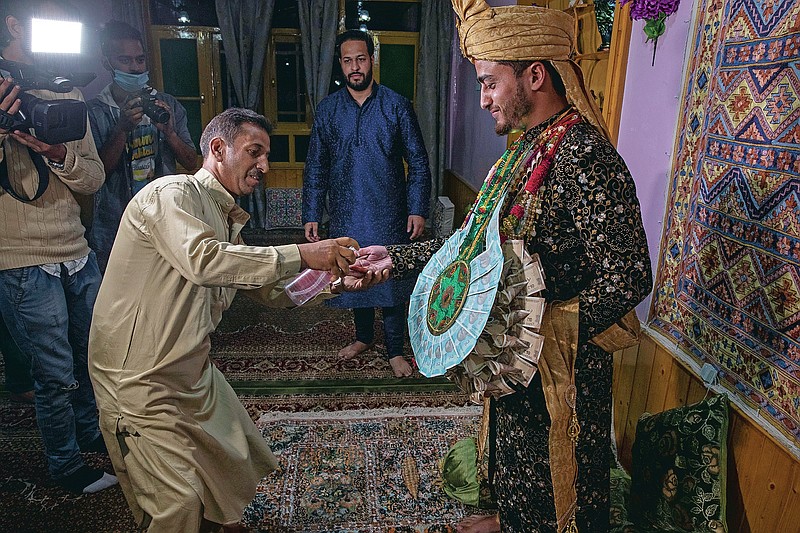 A Kashmiri man sprays sanitizer on the hand of Haseeb Mushtaq, a Kashmiri groom as he arrives at brides home during his wedding ceremony on the outskirts of Srinagar, Indian controlled Kashmir, Monday, Sept. 14, 2020. The coronavirus pandemic has changed the way people celebrate weddings in Kashmir. The traditional week-long feasting , elaborate rituals and huge gatherings have given way to muted ceremonies with a limited number of close relatives attending. With restrictions in place and many weddings cancelled, the traditional wedding chefs have little or no work. The virus has drastically impacted the life and businesses in the region. (AP Photo/ Dar Yasin)
