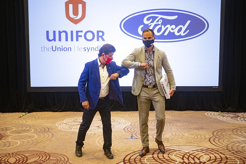 FILE  - In this Aug. 12, 2020 file photo, Unifor President Jerry Dias, left, elbow bumps Ryan Kantautas, Vice President of Human Resources at Ford Canada, after a photo opportunity at the start of formal contract talks with the Detroit Three automakers, Fiat Chrysler, Ford and General Motors, in Toronto. The union that represents Canadian auto workers says it has reached a tentative three-year contract deal with Ford to build five new electric vehicles at a factory near Toronto. Dias says the deal was reached early Tuesday, Sept. 22 after an all-night bargaining session.  (Chris Young/The Canadian Press via AP)