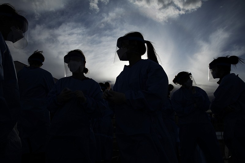 FILE - In this March 28, 2020, file photo, medical and physician assistant students wear personal protective equipment as they prepare to screen for possible coronavirus cases at a makeshift camp for the homeless in Las Vegas.  The U.S. death toll from the coronavirus topped 200,000 Tuesday, Sept. 22, a figure unimaginable eight months ago when the scourge first reached the world’s richest nation with its sparkling laboratories, top-flight scientists and towering stockpiles of medicines and emergency supplies. (AP Photo/John Locher, File)