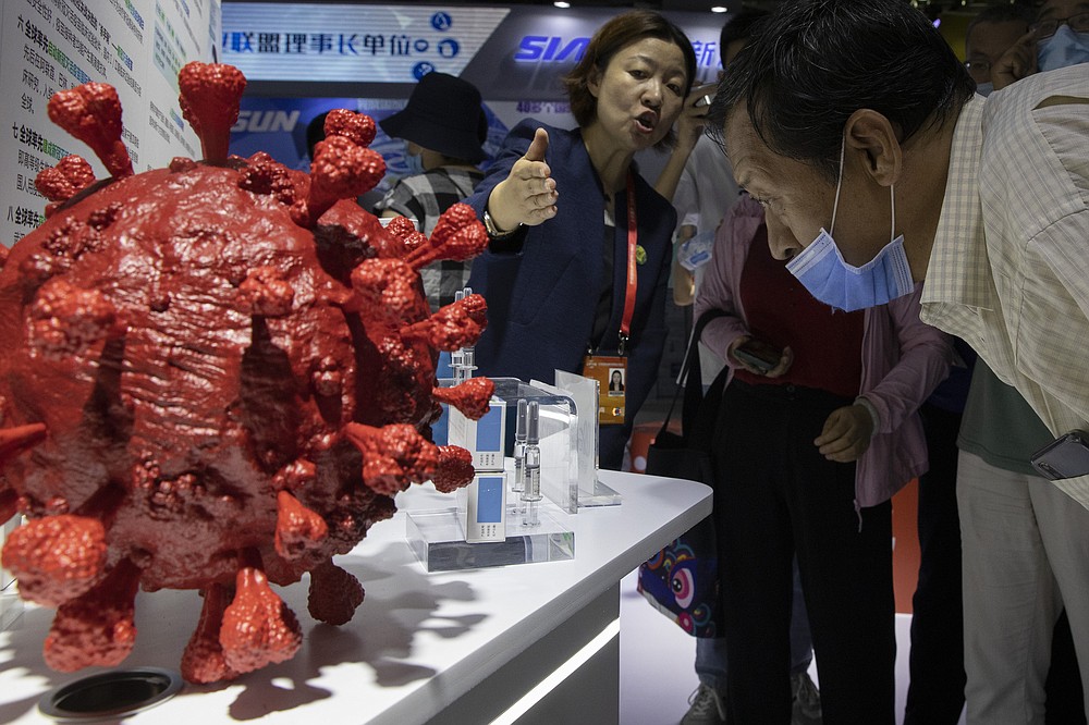 An employee answers questions from the public near samples of a COVID-19 vaccine produced by Sinopharm subsidiary CNBG are displayed during a trade fair in Beijing on Sunday, Sept. 6, 2020. State-backed Sinopharm's subsidiary CNBG has injected 350,000 people outside its clinical trials for COVID-19 vaccine, which have about 40,000 people enrolled. It's a highly unusual move that raises ethical and safety questions, as companies and governments worldwide race to develop a vaccine that will stop the spread of the new coronavirus. (AP Photo/Ng Han Guan)