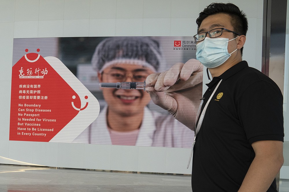 An employee of SinoVac stands near an advertisement for its SARS CoV-2 Vaccine for COVID-19 named CoronaVac at its factory in Beijing on Thursday, Sept. 24, 2020. SinoVac's CEO says they have injected 90 percent of its employees and family members, or about 3,000 people, and provided tens of thousands of rounds of CoronaVac to the municipal government of Beijing. It's a highly unusual move that raises ethical and safety questions, as companies and governments worldwide race to develop a vaccine that will stop the spread of the new coronavirus. (AP Photo/Ng Han Guan)
