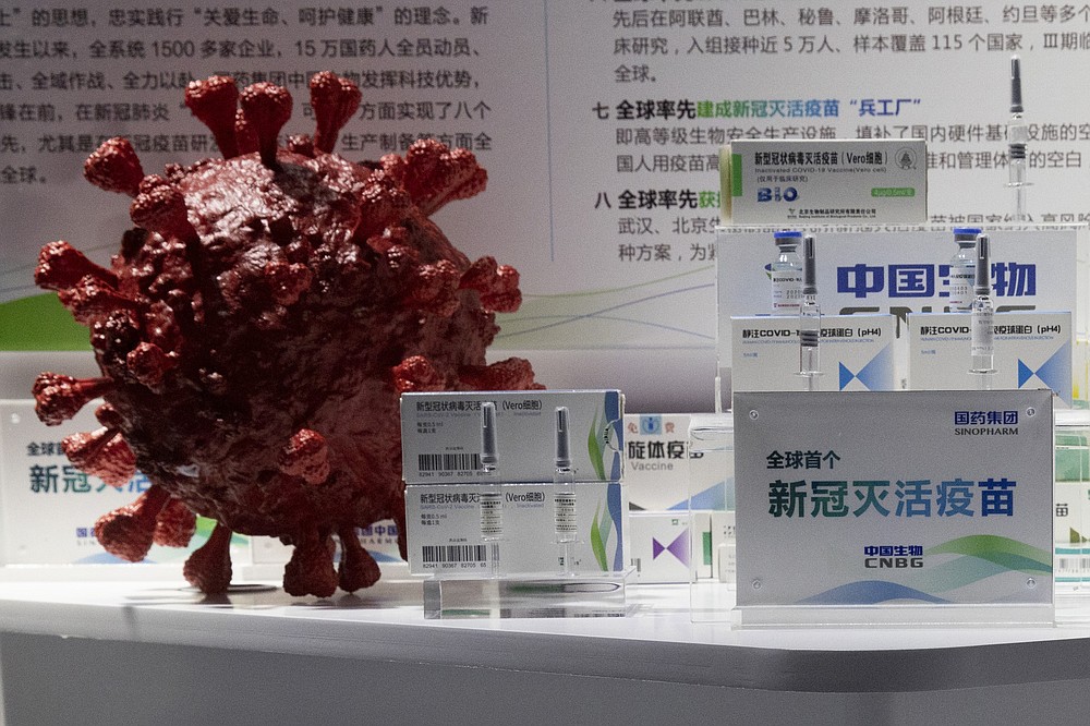 Samples of a COVID-19 vaccine produced by Sinopharm subsidiary CNBG are displayed near a 3D model of a coronavirus during a trade fair in Beijing on Sept. 6, 2020. State-backed Sinopharm's subsidiary CNBG has injected 350,000 people outside its clinical trials for COVID-19 vaccine, which have about 40,000 people enrolled. It's a highly unusual move that raises ethical and safety questions, as companies and governments worldwide race to develop a vaccine that will stop the spread of the new coronavirus. (AP Photo/Ng Han Guan)