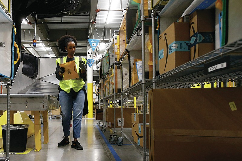 In this Dec. 17, 2019, photo Tahsha Sydnor stows packages into special containers after Amazon robots deliver separated packages by zip code at an Amazon warehouse facility in Goodyear, Ariz. 
(AP Photo/Ross D. Franklin)