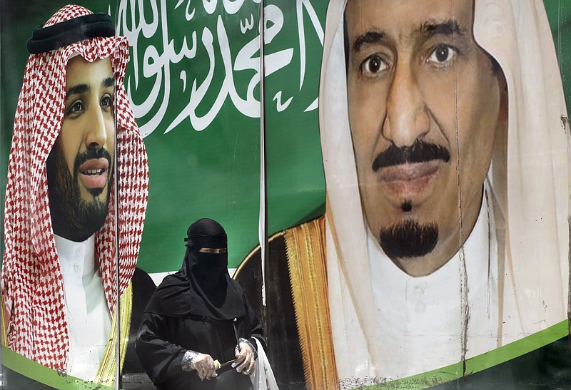 A woman walks past a banner showing Saudi King Salman, right, and his Crown Prince Mohammed bin Salman, outside a mall in Jiddah, Saudi Arabia, Monday, June 15, 2020. This was supposed to be Saudi Arabia's year to shine as host of the prestigious G20 gathering of world leaders. Instead, due to the coronavirus pandemic, the gathering this November will likely be a virtual meet-up, stripping its host of the pomp that would have accompanied televised arrivals on Riyadh's tarmac.  (AP Photo/Amr Nabil)