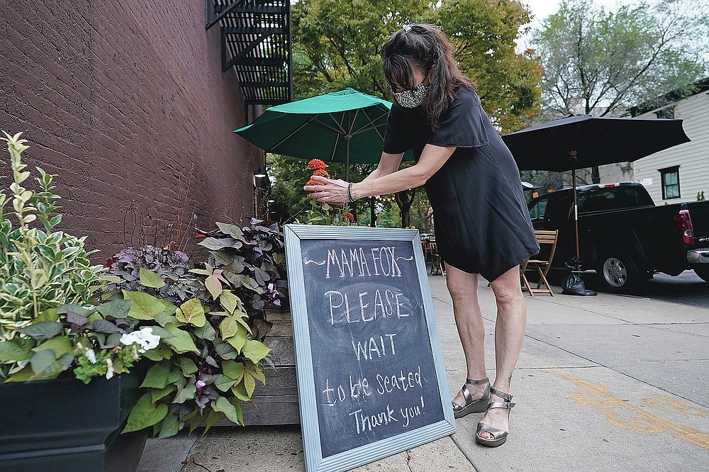 Samantha DiStefano adjusts flowers near the main entrance to Mama Fox, her Brooklyn bar and restaurant, Tuesday, Sept. 29, 2020, in New York, while preparing for indoor dining, which is permitted starting Wednesday in New York City. "We're all a little apprehensive, but that was the case when we started outdoor dining, too," said DiStefano. (AP Photo/Kathy Willens)