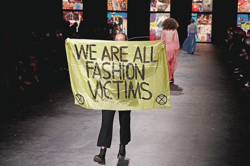 An activist displays a banner during Dior's Spring-Summer 2021 fashion collection presented Tuesday, Sept. 29, 2020 during the Paris fashion week. (AP Photo/Francois Mori)