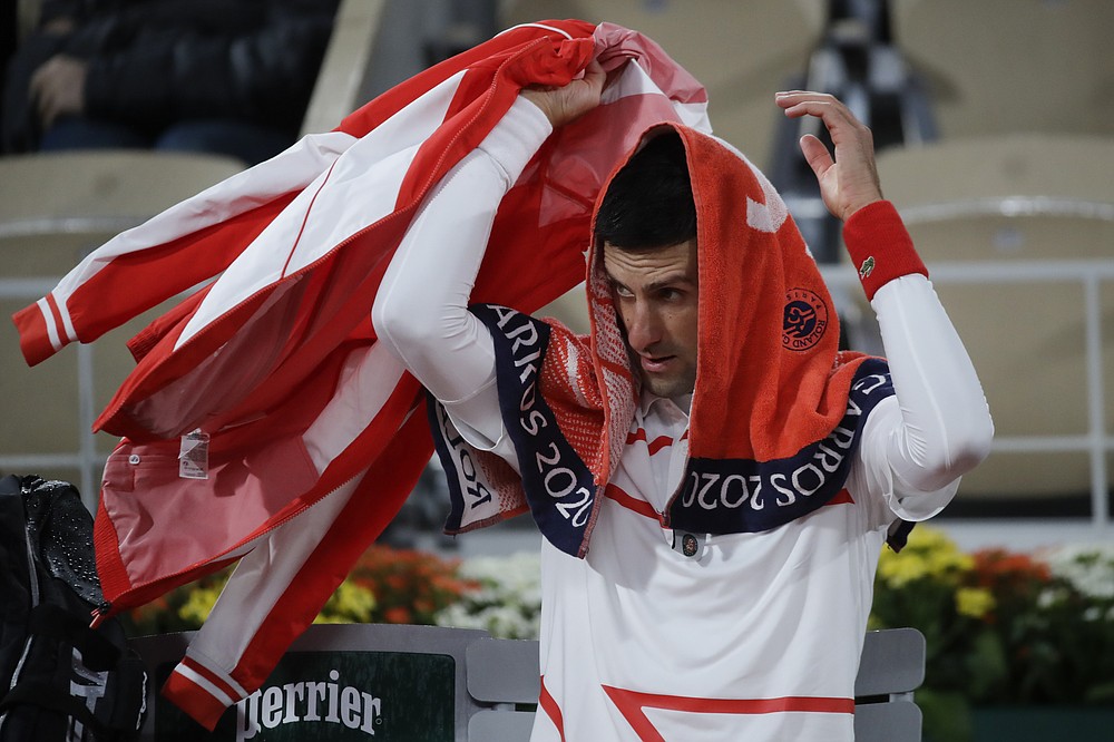 Serbia's Novak Djokovic cover himself in the rain as play was briefly suspended to close the roof of center court Philippe Chatrier in the third round match of the French Open tennis tournament against Colombia's Daniel Elahi Galan at the Roland Garros stadium in Paris, France, Saturday, Oct. 3, 2020. (AP Photo/Alessandra Tarantino)