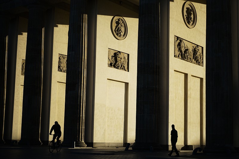 Two people pass the German landmark Brandenburg Gate early morning in Berlin, Germany, Monday, Sept. 28, 2020. (AP Photo/Markus Schreiber)