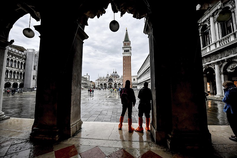 People wear waders as they observe St. Mark's Square during an expected high water, in Venice, northern Italy, Saturday, Oct. 3, 2020. Controversial and long-delayed underwater barriers passed their first emergency with flying colors on Saturday, protecting the Italian lagoon city of Venice from a tide that peaked at 130 centimeters (51-inches), a level that would normally inundate about half of the city. (Claudio Furlan/LaPresse via AP) story.lead_photo.caption