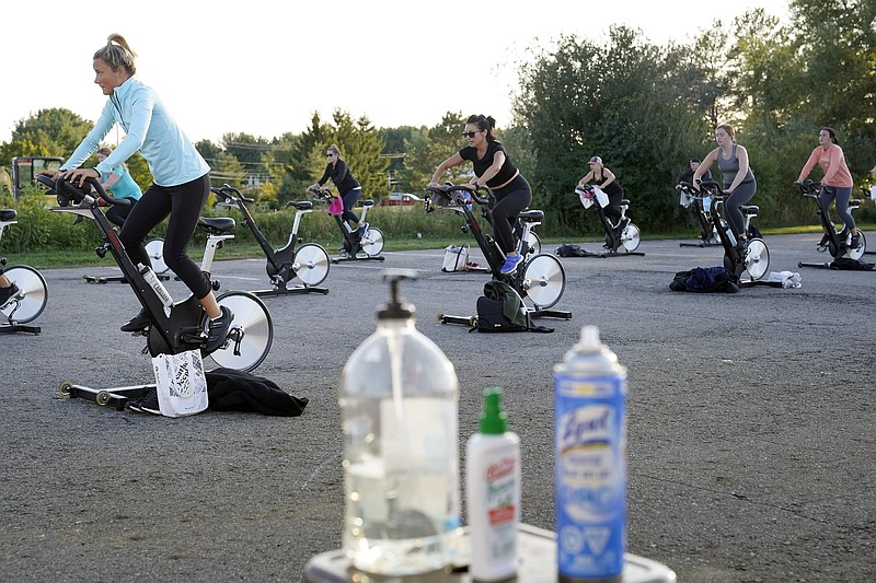 Jackie Brennan, of Merrimac, Mass., front left, pedals with others on stationary exercise bikes during a spinning class in a parking lot outside Fuel Training Studio, Monday, Sept. 21, 2020, in Newburyport. The gym's revenue is down about 60% during the COVID-19 pandemic. Fuel Training Studio plans to continue holding outdoor classes into the winter with the help of a planned greenhouse-like structure with heaters but no walls. (AP Photo/Steven Senne)