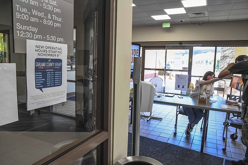 A sign, left, lists the new hours of the Garland County Library as Mallory Golden checks the temperature of a patron entering the building on Monday. - Photo by Grace Brown of The Sentinel-Record