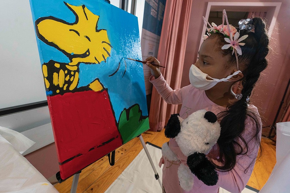Kaley Williams, 8, paints a panel of a "Peanuts" mural that will be placed in the outpatient pediatric floor of One Brooklyn Health at Brookdale Hospital, Thursday, Oct. 1, 2020, in the Brooklyn borough of New York. The virus pandemic won't stop Charlie Brown, Snoopy or the "Peanuts" gang from marking an important birthday and they're hoping to raise the spirits of sick kids while they celebrate. The beloved comic marks its 70th anniversary this week with new lesson plans, a new TV show and a philanthropic push that includes donating "Peanuts" murals for kids to paint in 70 children's hospitals around the globe, from Brooklyn to Brazil. (AP Photo/Mary Altaffer)