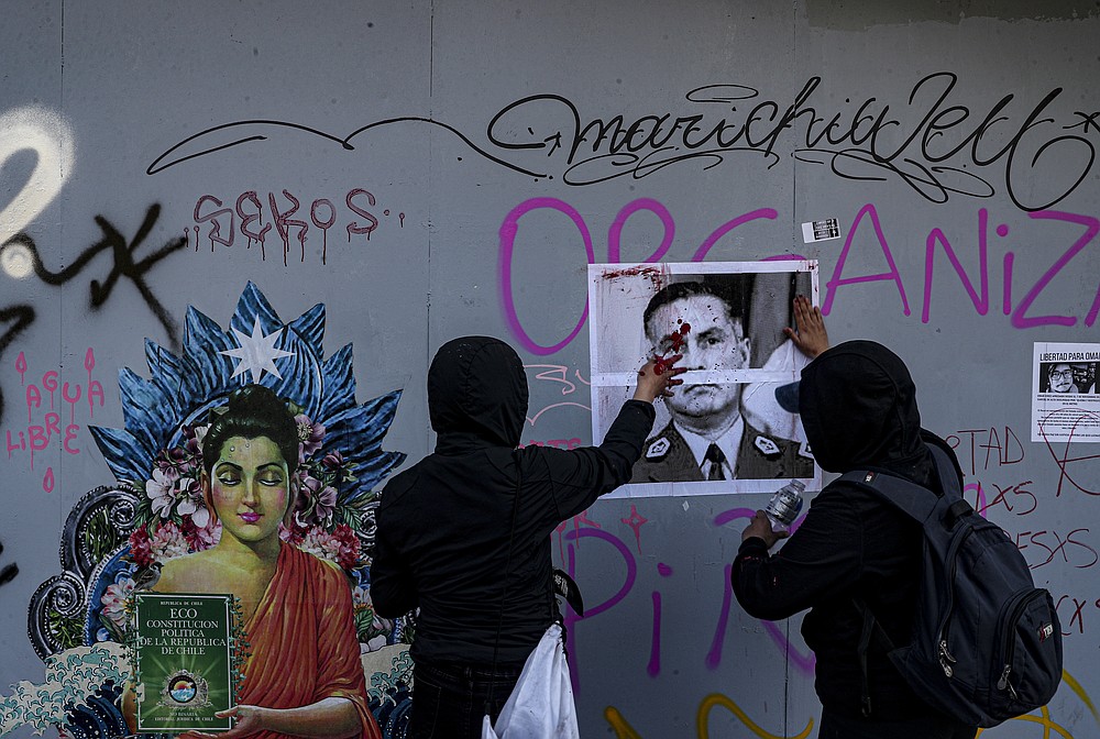 Demonstrators paste a portrait of National Police Chief Mario Rozas on the wall before painting it red to symbolize police brutality during a march against the commemoration of the discovery of the Americas, organized by Indigenous groups demanding autonomy and the recovery of ancestral land in Santiago, Chile, Monday, Oct. 12, 2020. (AP Photo/Esteban Felix)