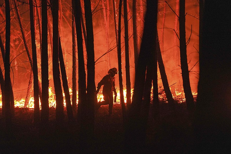 FILE - In this Monday, Sept. 14, 2020 file photo, a firefighter is silhouetted against a fire burning outside the village of Roqueiro, near Oleiros, Portugal. In the wake of heat waves, global warming, forest fires, storms, droughts and a rising number of hurricanes, the U.N. weather agency in a new report released Tuesday Oct. 13, 2020, is warning that the number of people who need international humanitarian help could rise 50% by 2030 compared to the 108 million who needed it in 2018 (AP Photo/Sergio Azenha, File)