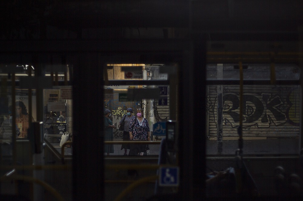 Women wearing face masks as a precautionary measure against the coronavirus wait for a bus next to closed shops in Tel Aviv, Israel, Tuesday, Oct. 13, 2020. Israel has had one of the largest income gaps and poverty rates among developed economies, even before the coronavirus pandemic. The country has a few high earners concentrated in the lucrative high-tech sector, while many Israelis barely get by as civil servants, in service industries or as small business owners. (AP Photo/Ariel Schalit)