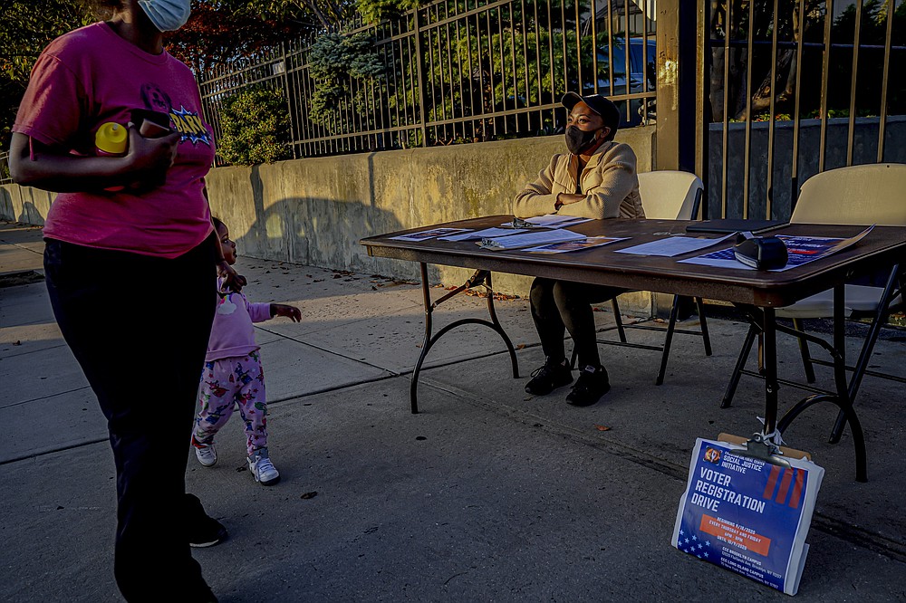 A woman and child walk past Laurae Caruth, right, volunteer with Christian Cultural Center Social Justice Initiative's voter registration drive, as she sits at a table where she registers voters, Friday, Sept. 18, 2020, in the Brooklyn borough of New York. "I'm out here volunteering because of how important it is to exercise the right to vote," Caruth said. In recent election cycles, predominantly Black congregations across the country have launched get-out-the-vote campaigns commonly referred to as “souls to the polls.” But instead of packing buses and vans to shuttle people to early voting sites this year, church leaders say they are organizing caravans for absentee ballot drop-offs and in-person early voting. (AP Photo/Bebeto Matthews)