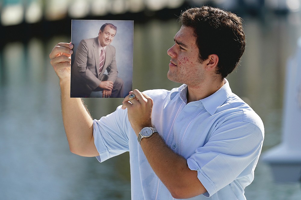 Freddy Vallejo Jr. holds a photograph of his grandfather Jorge Vallejo, Saturday, Sept. 26, 2020, at the family vacation home in Key Largo, in the Florida Keys. Jorge Vallejo, a retired OB-GYN, and his son Carlos Vallejo, who practiced internal medicine, died of the coronavirus within weeks of one another in South Florida. (AP Photo/Lynne Sladky)