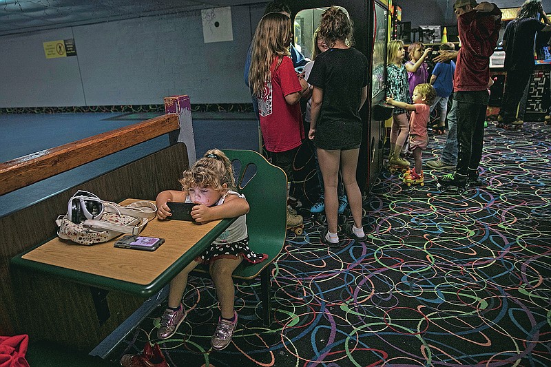 A girl is immersed in a smartphone game while others play in an arcade at a skating rink, Saturday, Aug. 1, 2020, in Anna, Ill. (AP Photo/Wong Maye-E)