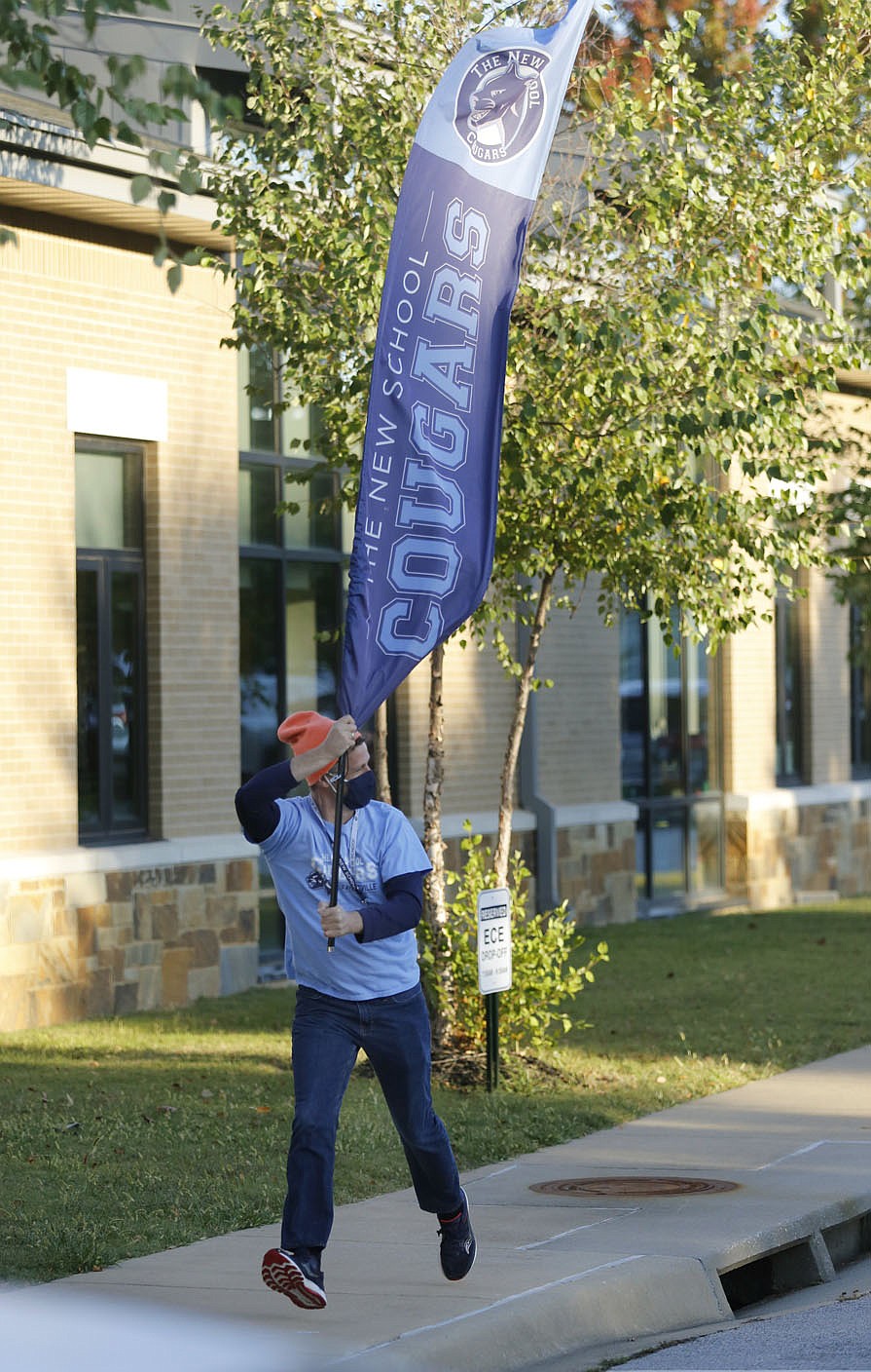 Troy Schremmer, early childhood music teacher at The New School, runs with a banner as he greets the students on Thursday, October 1, 2020, as they are dropped off at the school for a day of classes in Fayetteville. Visit nwadg.com/photos for a photo gallery. (NWA Democrat-Gazette / David Gottschalk)