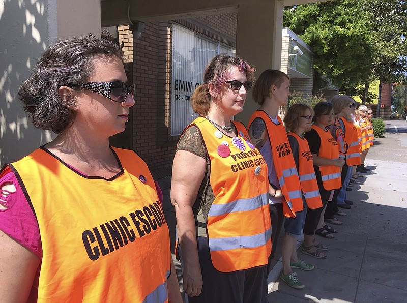 FILE - In this July 17, 2017 file photo, escort volunteers line up outside the EMW Women's Surgical Center in Louisville, Ky., the state's only abortion clinic. Kentucky's Attorney General Daniel Cameron, an anti-abortion supporter, said Friday, March 27, 2020, that abortions should cease as part of the governor's order halting elective medical procedures in the state due to the coronavirus pandemic. (AP Photo/Dylan Lovan, File)