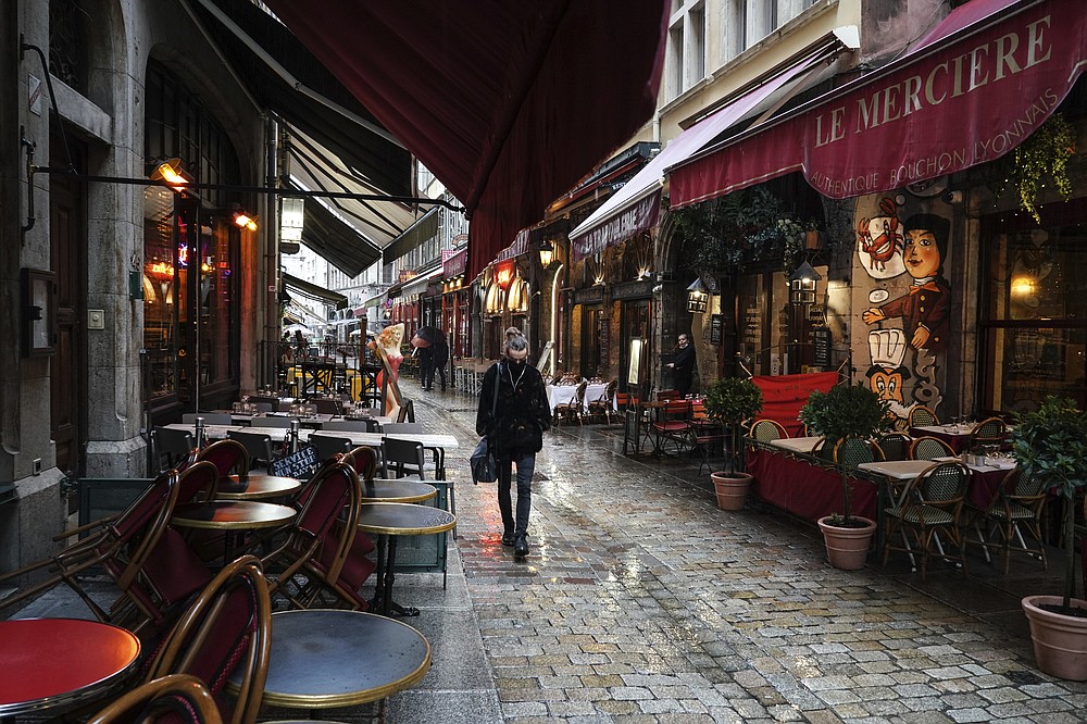 FILE - In this Friday, Oct. 2, 2020 file photo, a woman walks by empty restaurants in the center of Lyon, central France. Europe’s economy was just catching its breath from what had been the sharpest recession in modern history. A resurgence in coronavirus cases this month, Oct. 2020, risks undoing that and will likely turn what was meant to be a period of healing for the economy into a lean winter of job losses and bankruptcies. (AP Photo/Laurent Cipriani, File)