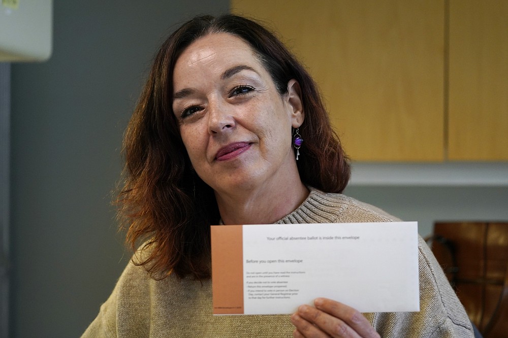 In this Friday, Oct. 16, 2020, photo undecided voter Tracye Stewart holds her official Virginia ballot in her office in Richmond, Va., Friday Oct. 16, 2020. Stewart, who voted for Donald Trump in 2016, said that she’s more ideologically in line with Trump than Democratic presidential candidate former Vice President Joe Biden. But her regular, and sometimes tearful, conversations with a friend she’s known since 3rd grade has given her pause.  Stewart’s ballot remains on her desk at home unfilled. (AP Photo/Steve Helber)
