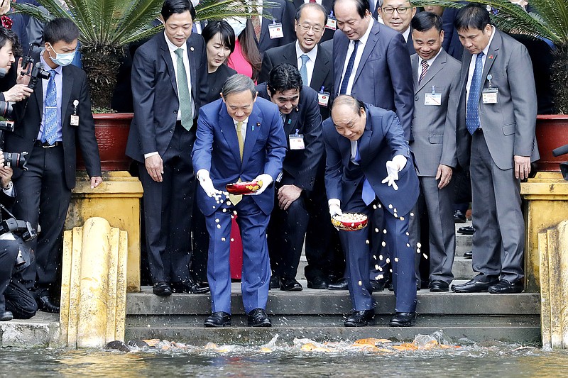 Japanese Prime Minister Yoshihide Suga, center left, and his Vietnamese counterpart Nguyen Xuan Phuc, center right, feed the fish by a pond at the Presidential Palace compound in Hanoi, Vietnam, Monday, Oct. 19, 2020. Suga is on an official visit to Vietnam. (AP Photo/Minh Hoang, Pool)