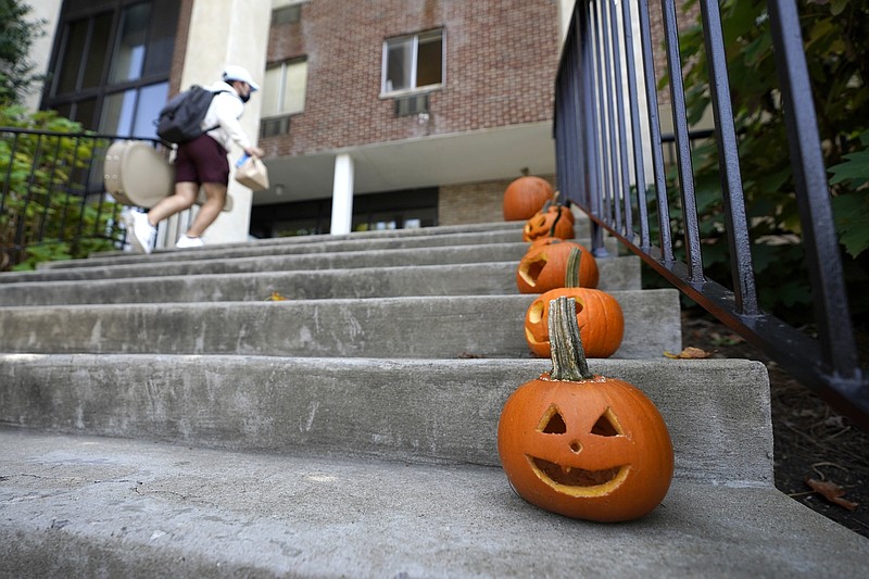A man wears a face mask to protect against COVID-19 while walking near Jack-o'-lanterns line up on steps at Belmont University, the site of the final presidential debate between Republican President Donald Trump and Democratic candidate former Vice President Joe Biden, Tuesday, Oct. 20, 2020, in Nashville, Tenn. The debate is scheduled for Thursday, Oct. 22. (AP Photo/Julio Cortez)
