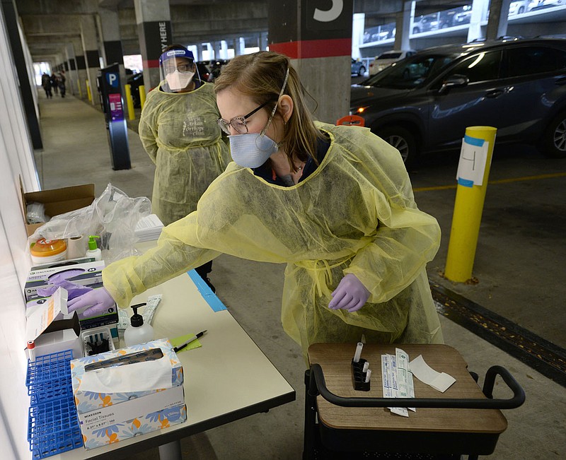 Roxana Hutchcroft (right), an RN with Arkansas Foundation of Medical Care and the Arkansas Department of Health, collects testing supplies Friday before administering a covid-19 test for a member of the University of Arkansas campus community inside the Garland Avenue parking garage on the university campus in Fayetteville. (NWA Democrat-Gazette/Andy Shupe)