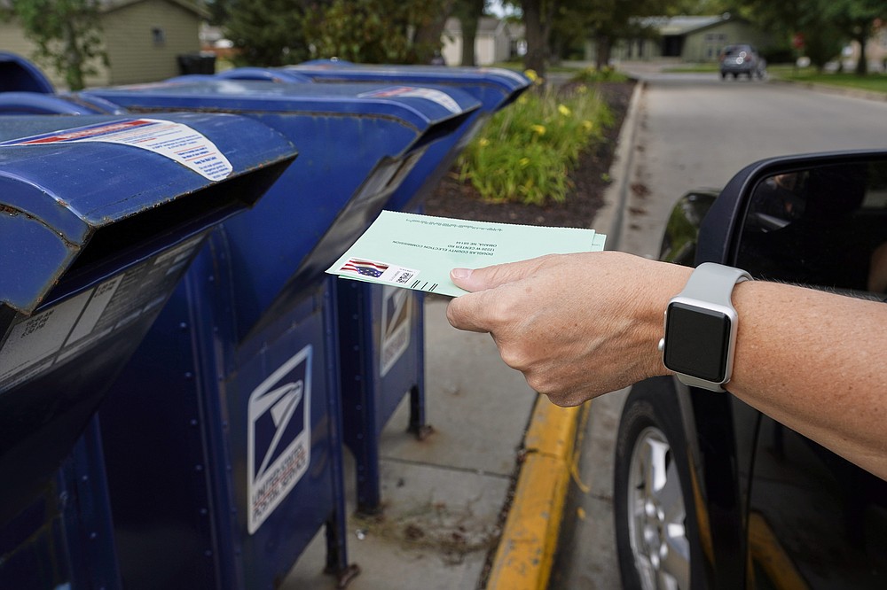 FILE - In this Aug. 18, 2020, file photo, a person drops applications for mail-in-ballots into a mailbox in Omaha, Neb. U.S. Postal Service records show delivery delays have persisted across the country as millions of Americans began voting by mail, raising the possibility of ballots being rejected because they arrive too late. Postal data covering the beginning of October show nearly all of the agency's delivery regions missing agency targets of having more than having more than 95% of first-class mail arrive within five days. (AP Photo/Nati Harnik, File)