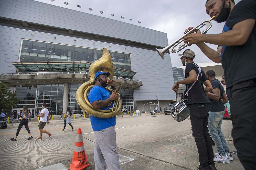 Members of the Rebirth Brass Band, from left, tuba player Clifton Smith, drummer Jenard Andrews, bass drummer Thaddeus Ramsey, and trumpet player Glenn Hall, stand across the street from the Smoothie King Center playing songs for the long line of early voters standing outside the sport complex in New Orleans, Tuesday, Oct. 27, 2020. (Chris Granger/The Advocate via AP)