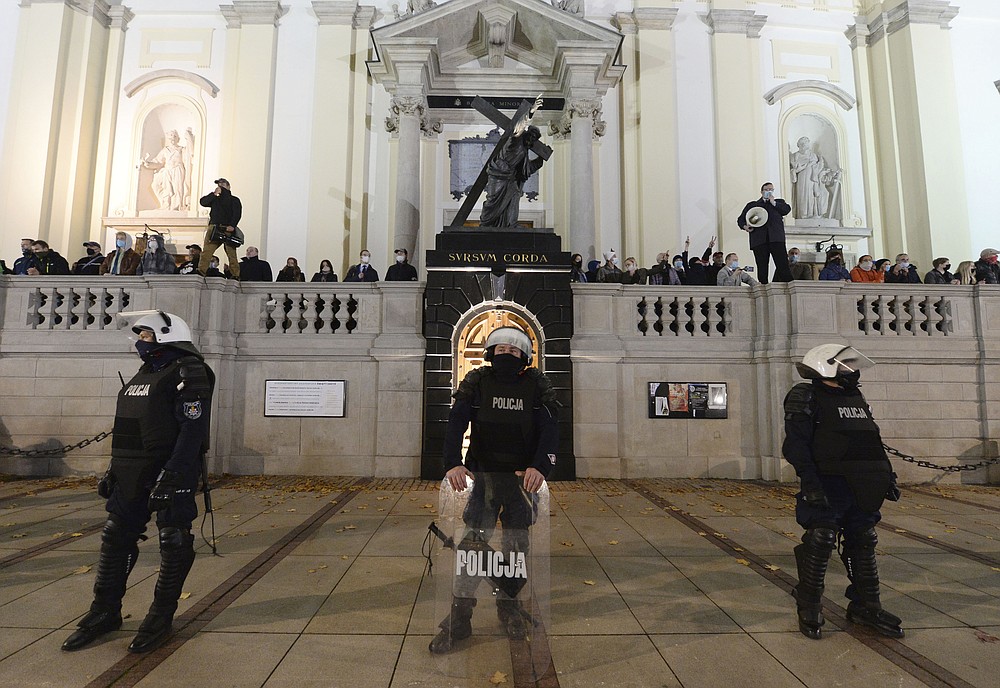Members of a far-right organization stand guard in front of the Holy Cross Church, fronted by a row of police officers, in Warsaw, Poland, Wednesday Oct. 28, 2020. The far-right group members vowed to defend churches after protesters angry over an abortion ban disrupted Masses and spray-painted churches last Sunday. (AP Photo/Czarek Sokolowski)
