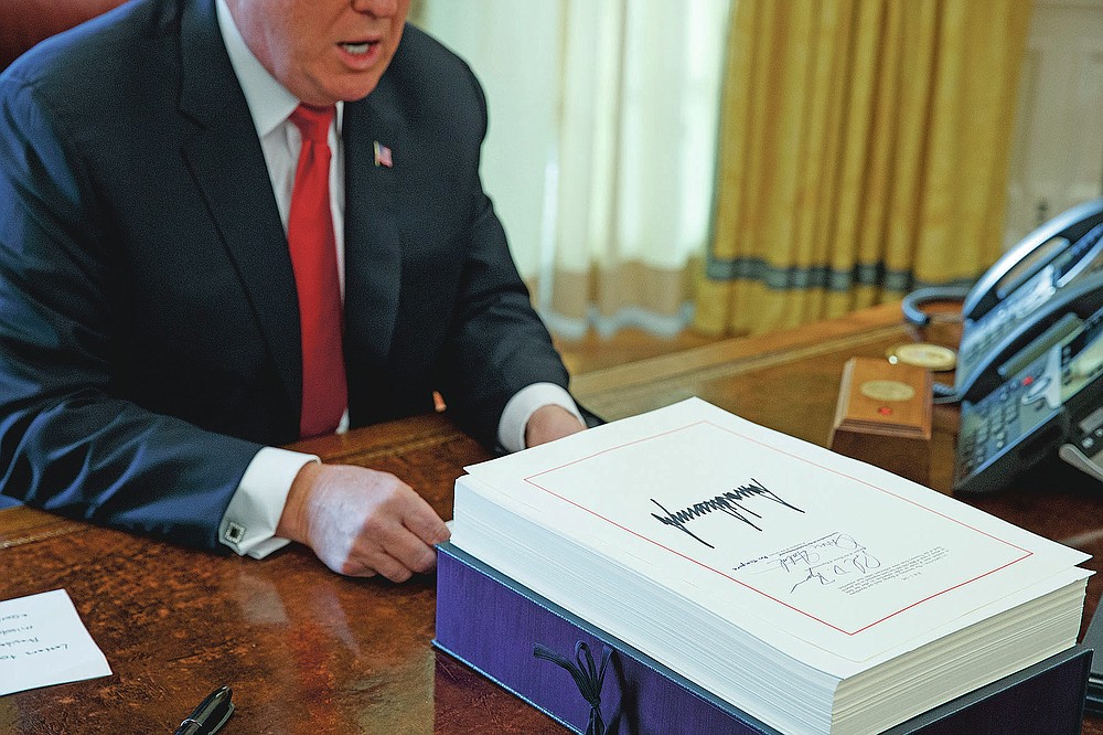 FILE- In this Dec. 22, 2017, file photo President Donald Trump speaks with reporters after signing the tax bill and continuing resolution to fund the government, in the Oval Office of the White House in Washington. On Friday, Oct. 30, 2020, The Associated Press reported on stories circulating online incorrectly asserting that by reversing Trump’s tax cuts, Democratic presidential nominee Joe Biden would raise taxes on 82% of Americans. Biden says he won’t raise taxes on anyone making less than $400,000. (AP Photo/Evan Vucci, File)