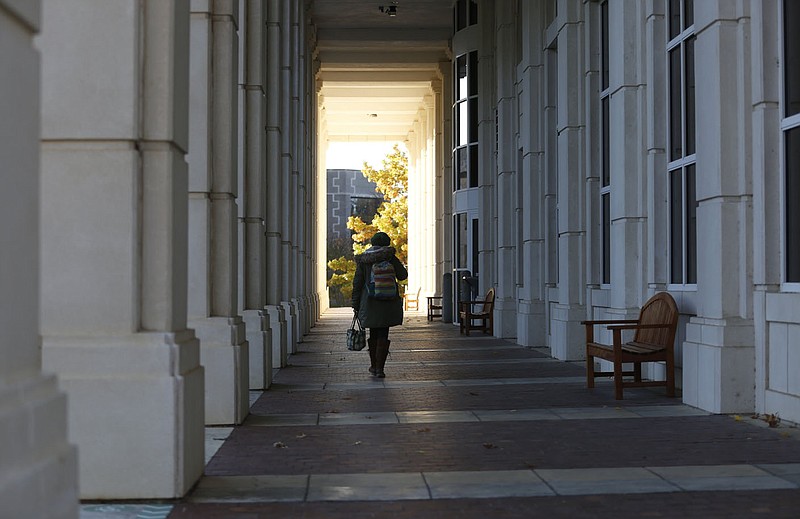 A pedestrian walks Friday, October 30, 2020, in the direction of the sunlight at the end of the tunnel formed by the columns on the east side of David W. Mullins Library on the campus of the University of Arkansas in Fayetteville. Built in 1968, Mullins Library replaced Vol Walker Hall as the main University Library. Check out nwaonline.com/201031Daily/ and nwadg.com/photos for a photo gallery.(NWA Democrat-Gazette/David Gottschalk)