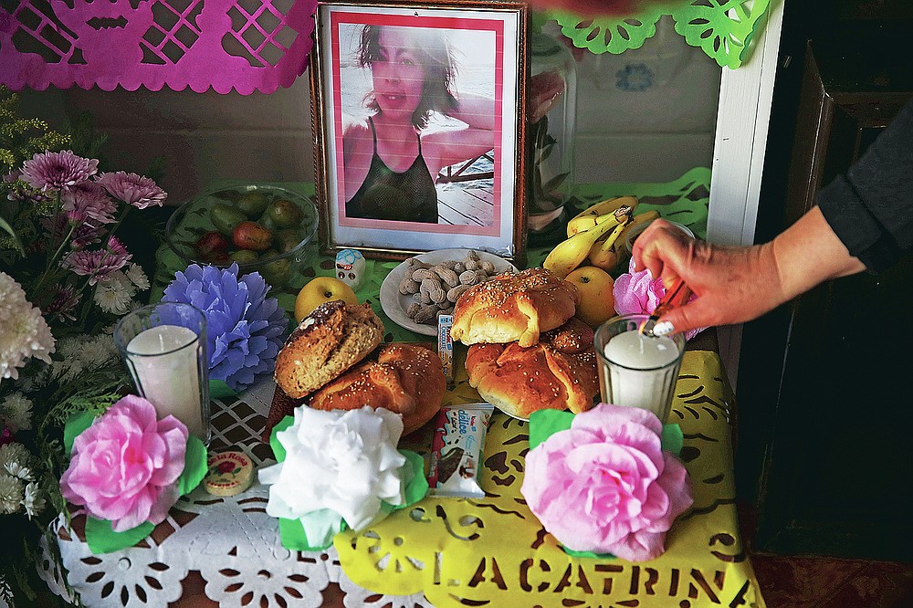 Eulogia Herrera lights candles on a Day of the Dead altar featuring pictures of her daughter Mariana Luna Herrera who she said died of complications related to COVID-19, and who also had leukemia, at their home in Valle de Chalco on the outskirts of Mexico City, Friday, Oct. 30, 2020. Mexican families traditionally flock to local cemeteries to honor family members who died as part of the "Day of the Dead" holiday, every Nov. 1 and 2, but according to authorities cemeteries will be closed this year to help slow the spread of COVID-19. (AP Photo/Marco Ugarte)