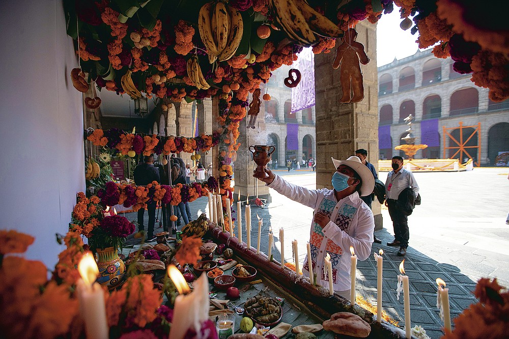 A man, wearing a protective face mask amid the new coronavirus, burns incense during a Day of the Dead ceremony at the Mexico's presidential palace in Mexico City, Saturday, Oct. 31, 2020. The weekend holiday isn't the same in a year so marked by death in a country where more than 90,000 people have died of COVID-19, many cremated rather than buried and with cemeteries forced to close. (AP Photo/Fernando Llano)