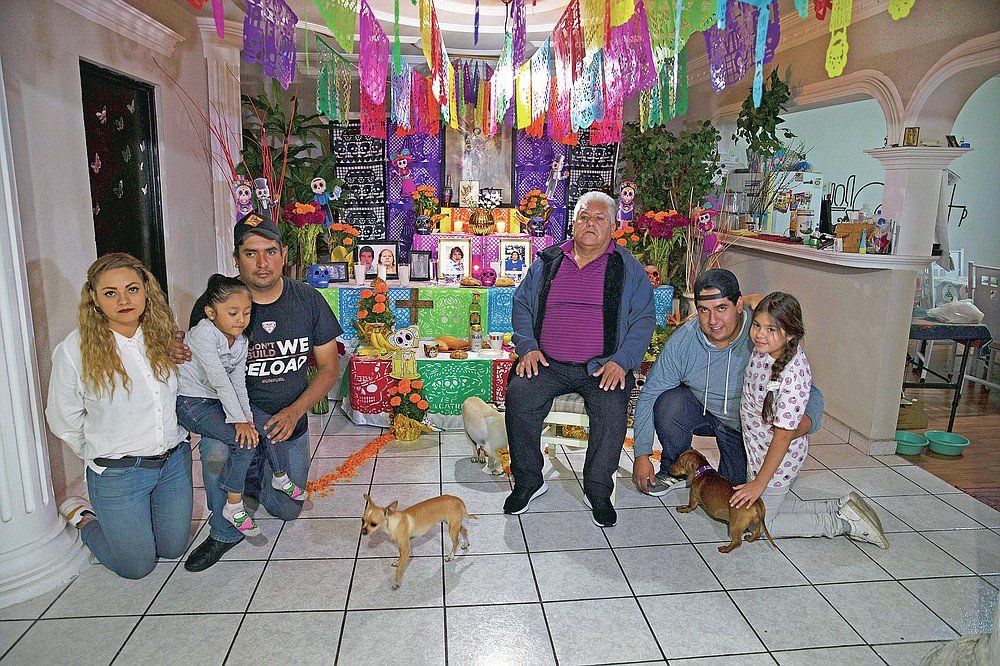 Salvador Cervantes Torres, center, a recovered COVID-19 patient, and his family pose for photos on a Day of the Dead altar for his wife Ivone Guadalupe Lozano Garcia and his mother in law Silvina Garcia, who died of complications related to coronavirus, at their home in Ecatepec, Mexico, Saturday, Oct. 31, 2020. Mexican families traditionally flock to local cemeteries to honor family members who died as part of the "Day of the Dead" holiday, every Nov. 1 and 2, but according to authorities cemeteries will be closed this year to help slow the spread of COVID-19. (AP Photo/Marco Ugarte)