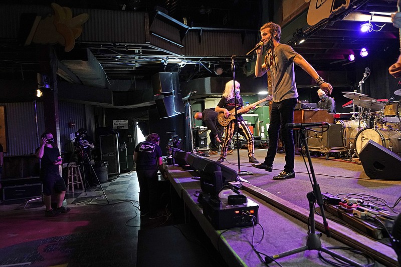 In this Oct. 26, 2020, photo, David Shaw, foreground, frontman for the band The Revivalists, performs with actor Harry Shearer, co-author and character in the movie "This Is Spinal Tap," as they record a video stream concert with the band Galactic, inside an empty Tipitina's music club, in New Orleans. Music clubs all over the nation — pop culture icons like the Troubadour in West Hollywood, the Bluebird Cafe in Nashville, The Bitter End in New York's Greenwich Village — are shuttered due to the coronavirus. And owners fear for the future of their businesses and of a musical way of life. (AP Photo/Gerald Herbert)